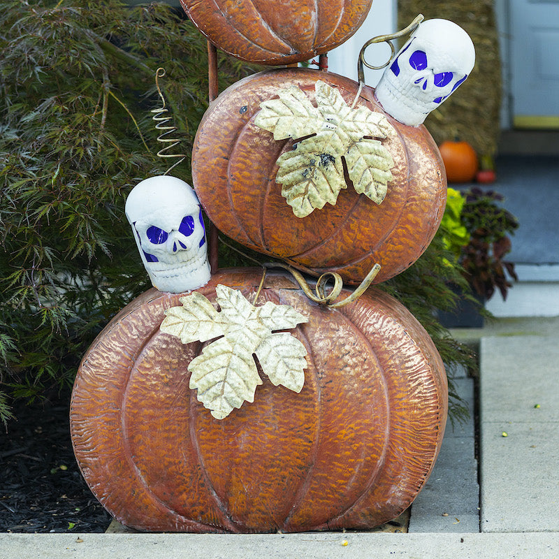 Close up of orange pumpkins with gold maple leafs. Pumpkins also topped with skull heads with purple lit eyes on battery pack.