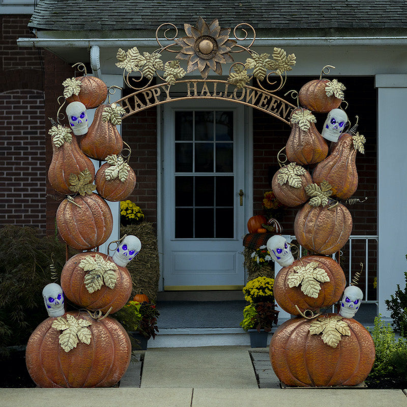 Halloween archway with happy halloween wording, orange pumpkins with gold leaves, and skulls lit with purple lights.