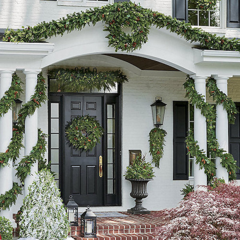 Beautiful green garland with lights and pinecones decorating outdoor area.