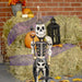 Front view of skeleton soldier with pumpkin staff in hand. Hanging bat in other hand. Skull shoulders and black soldier coat.